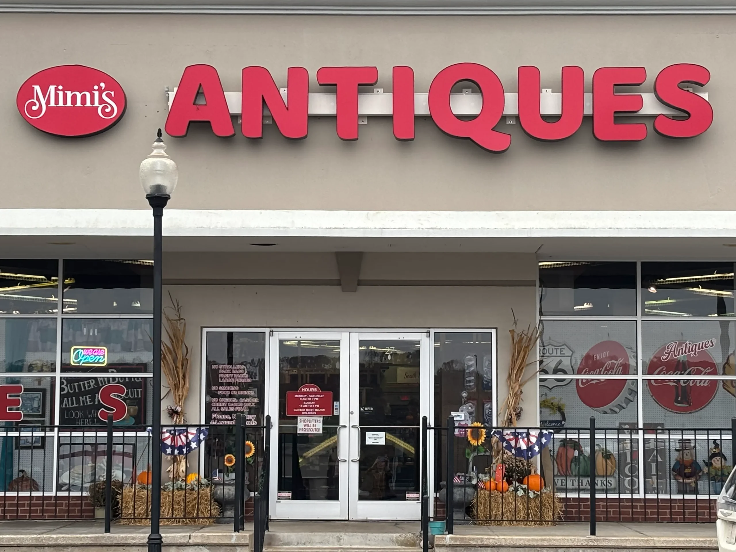 Mimi's Antiques storefront features large glass windows displaying various items, with bold red signage reading OPEN and ANTIQUES